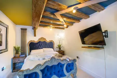 a bedroom with a blue bed and a flat screen tv at Executive Suite with Private HotTub, Full SkyTV in 600 Year Old Manor House in Saffron Walden