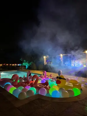 a group of people swimming in a pool at night at Grade II Listed Farmhouse, Pool, Hot Tub, Games Room, Celebration Hall, Car Park, 10ppl, 45 min from Central London in Stapleford Tawney