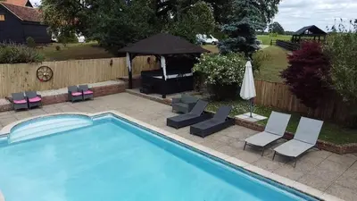 a swimming pool with chairs and an umbrella at Grade II Listed Farmhouse, Pool, Hot Tub, Games Room, Celebration Hall, Car Park, 10ppl, 45 min from Central London in Stapleford Tawney