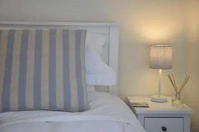 a bed with a striped pillow and a lamp on a night stand at 1 Tailors Cottage, Woodbridge in Woodbridge