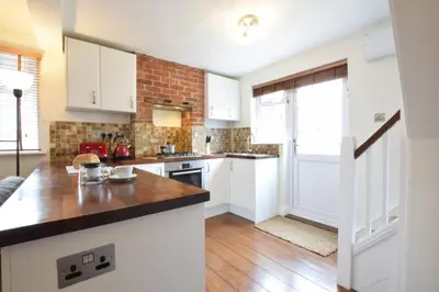 a kitchen with white cabinets and a brick wall at 1 Tailors Cottage, Woodbridge in Woodbridge