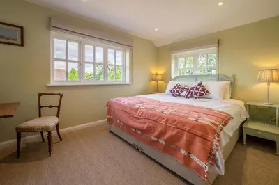 a bedroom with a bed and a chair and windows at Foxhole Cottage in Stowmarket