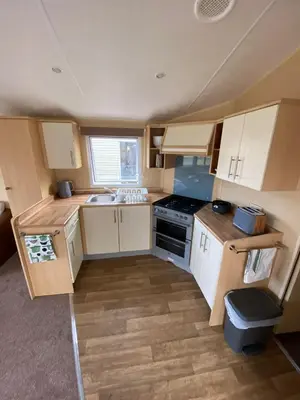 a small kitchen with white cabinets and a stove at 1 Martello Beach 8 berth holiday home with pools in Clacton-on-Sea