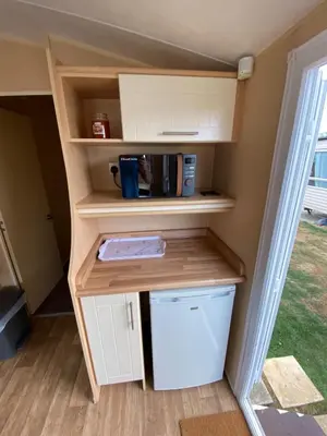 a small kitchen with white cabinets and a shelf at 1 Martello Beach 8 berth holiday home with pools in Clacton-on-Sea