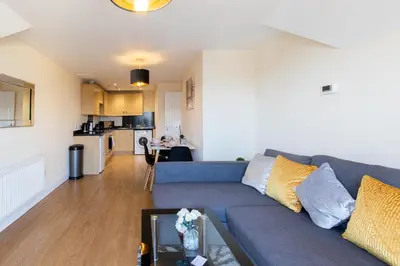 a living room with a blue couch and a kitchen at Velvet 1-bedroom penthouse, Clockhouse, Hoddesdon in Hoddesdon