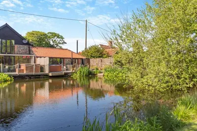 a house sitting next to a body of water at Tilly's, a two bedroom holiday retreat with hot tub and views of the pond in Barningham
