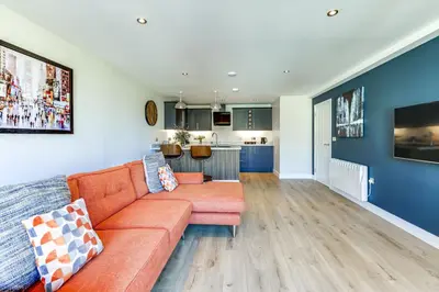 a living room with a orange couch and a kitchen at The Old Warehouse Ely in Ely