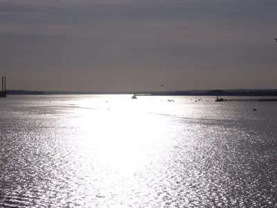 a large body of water with the sun shining on it at Tidal Walk in Harwich