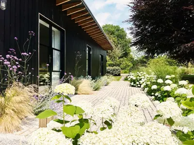 a garden with white flowers next to a black building at Little Owl by The Suffolk Cottage Collection in Aldeburgh