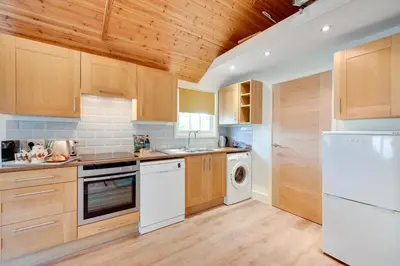 a kitchen with wooden cabinets and a white dishwasher at 1 Bed in Debenham oc-glah in Worlingworth