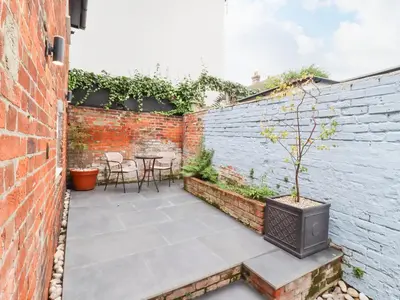 a patio with a brick wall and a table with a tv at Wherry Cottage in Manningtree