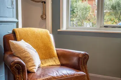 a brown leather chair with a yellow throw pillow at Tipple Cottage in Peasenhall