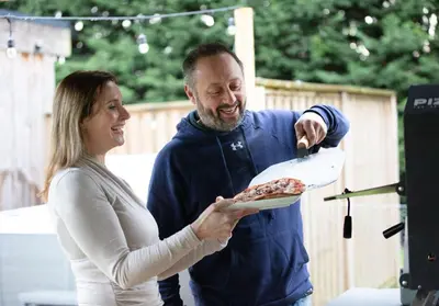 a woman holding a plate of pizza with a man at City to Country Retreat Luxury Lodges with Hot Tub, BBQ, Fire Pit in Toppesfield