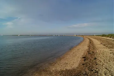 a sandy beach with water and boats in the distance at Secluded Island Retreat - in the heart of the Anchorage in West Mersea