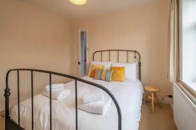 a bedroom with a bed with white sheets and yellow pillows at 40 Buller Road - Aldeburgh Coastal Cottages in Leiston