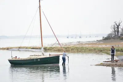 a man standing in the water next to a sail boat at Upper Lodge, Shotley in Chelmondiston