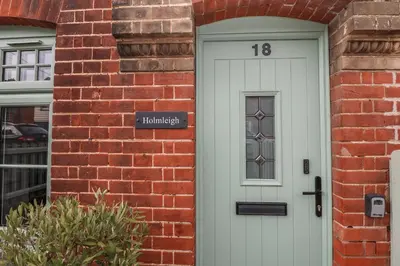 a brick house with a white door with a sign on it at Holmleigh, Aldeburgh in Aldeburgh