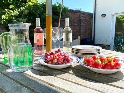 a table with plates and bowls of strawberries and wine bottles at Seawall Cottage, Aldeburgh in Aldeburgh