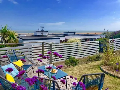 a patio with a table with purple flowers and the beach at Aldeburgh Lodge Gardens in Aldeburgh