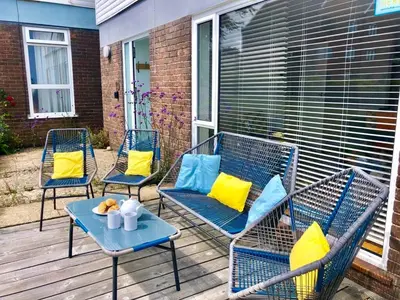three chairs with yellow and blue pillows on a porch at Aldeburgh Lodge Gardens in Aldeburgh