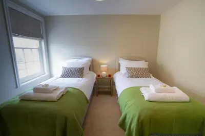 a bedroom with two beds with green sheets and a window at 10 Church Walk, Aldeburgh in Aldeburgh