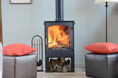 a stove with a fire in a living room with two couches at Manor House Barn, Peasenhall in Peasenhall