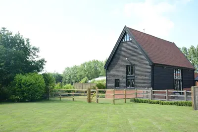 a black barn with a fence in front of it at Manor House Barn, Peasenhall in Peasenhall