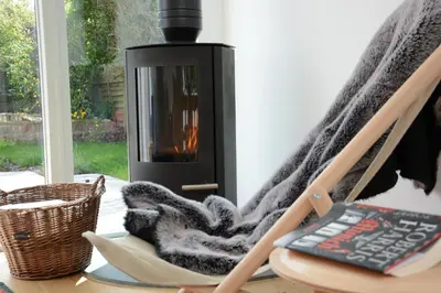 a blanket sitting on a chair next to a fireplace at 2 Pink Cottages, Aldeburgh in Aldeburgh