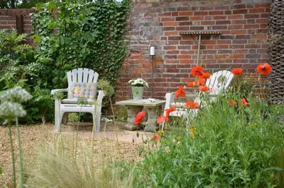 a garden with two chairs and a table and flowers at The Nookery at Snape Hall in Snape