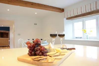a plate of grapes and cheese and two glasses of wine at Woodland Cottage, Great Glemham in Framlingham