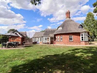 a large brick house with a thatched roof at The Round House in Kettleburgh