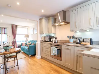 a kitchen with white cabinets and a table and a couch at 51 Tern Cottage, Aldeburgh in Aldeburgh