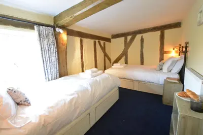 two beds in a room with wooden beams at The White House with Studio in Homersfield