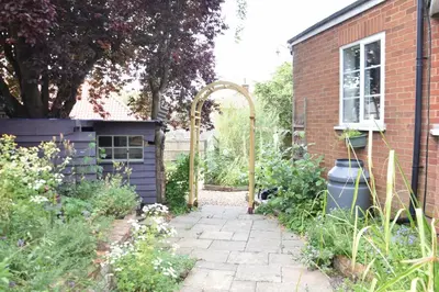 a garden with an arbor and a brick house at Rosedene, Rickinghall in Rickinghall
