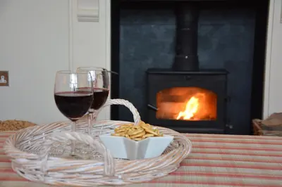 a table with a glass of wine and a basket of food and a fireplace at Tamarisk, Aldeburgh in Aldeburgh