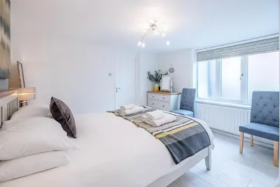 a white bedroom with a bed and a blue chair at The Apartment at Clare House, Aldeburgh in Aldeburgh