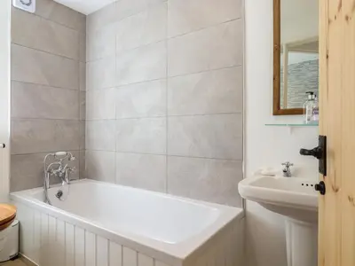 a white bathroom with a tub and a sink at Warren Cottage in Leavenheath