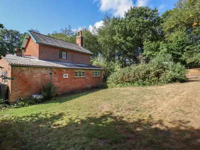 an old brick house on a grass field at Warren Cottage in Leavenheath