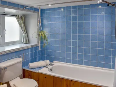 a blue tiled bathroom with a tub and a toilet at The Old Butcher's Shop in Wereham