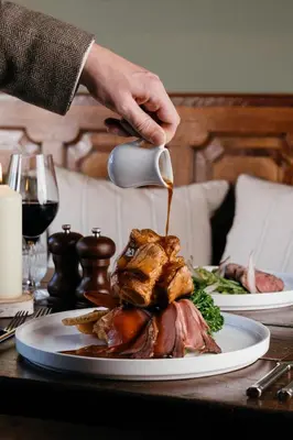 a person is pouring gravy on a plate of food at The Crown, Bildeston in Bildeston