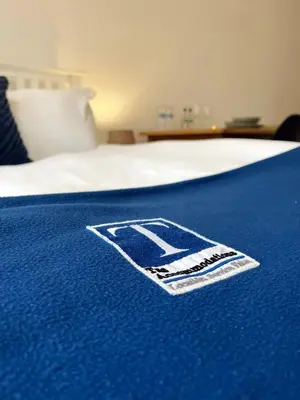 a blue blanket with a logo on top of a bed at Cambridge Studios and Suites by Tas Accommodations in Cambridge