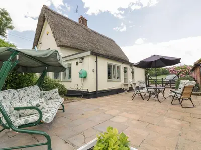 a patio with chairs and umbrellas in front of a house at Waveney Cottage in Diss
