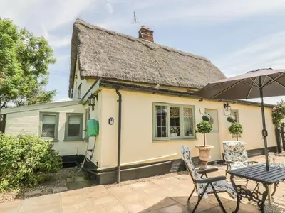 a yellow cottage with a table and an umbrella at Waveney Cottage in Diss