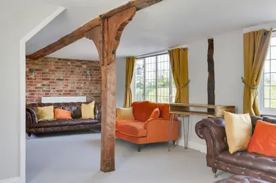 a living room with leather furniture and a brick wall at Beautiful thatched Dynes Cottage Finchingfield sleeps 10 in Finchingfield
