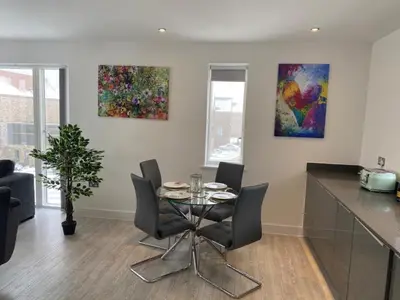 a dining room with a table and chairs and paintings at Exquisite & Contemporary 2 Bed Apartment w Parking 10 mins walk to Papworth, Addenbrookes hospitals & Bio Medical Campus in Trumpington