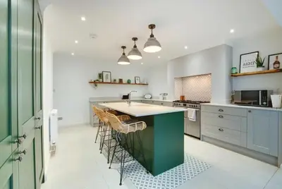 a kitchen with a green island with chairs in it at Belle Vue Cottage in Downham Market