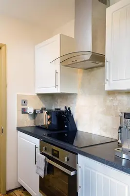 a kitchen with white cabinets and a black appliance at Deluxe 2 Bed Versace Bungalow Hot Tub, Sky TV, Cinema Screen Saffron Walden in Saffron Walden