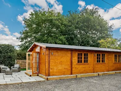 a wooden shed with a patio in a yard at Hulver Lodge, Snape, Suffolk. in Snape