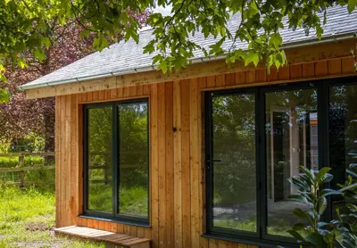 a wooden cabin with glass doors in a garden at The Weeping Willow in Bury Saint Edmunds