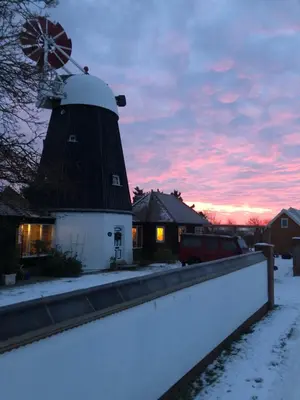 a barn with a windmill in the snow at sunset at The Millers Cottage in Cambridge